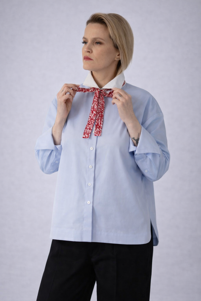 Model wearing a light blue long-sleeve button-up shirt with a contrast white collar, soft drape, and relaxed silhouette designed for effortless polish.