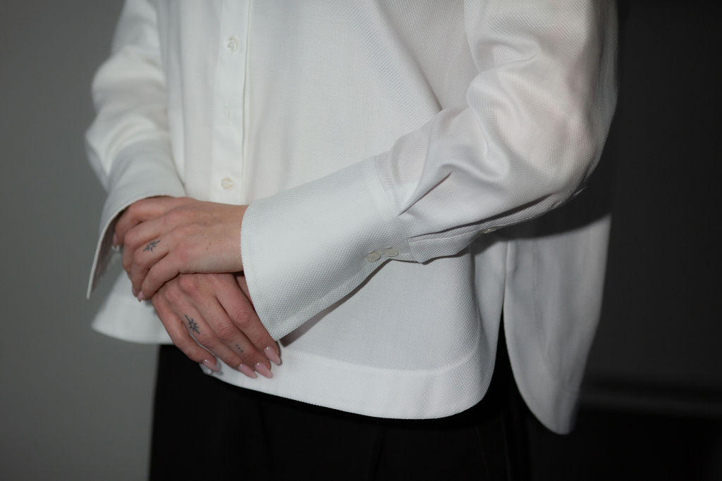 Model wearing a white long-sleeve button-up shirt featuring a sharp collar, clean front buttons, and an easy, relaxed fit for a polished everyday look.